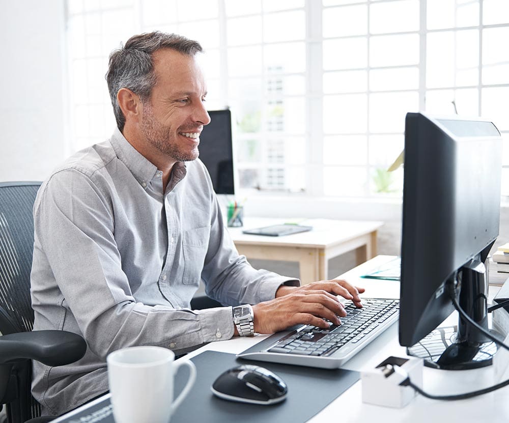 Trader's Classroom from Elliott Wave International. Man sitting at computer smiling.